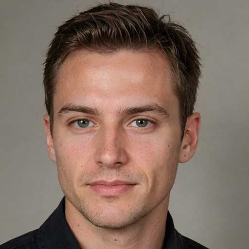 A young man with short brown hair and a beard is looking directly at the camera against a plain gray background.